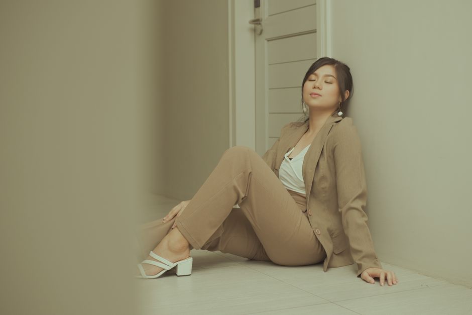 Businesswoman in a beige suit relaxing against a wall in a hallway, exemplifying modern fashion.