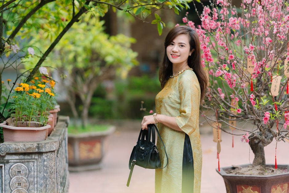 Elegant woman in traditional attire posing outdoors with blooming trees, exuding cultural charm.