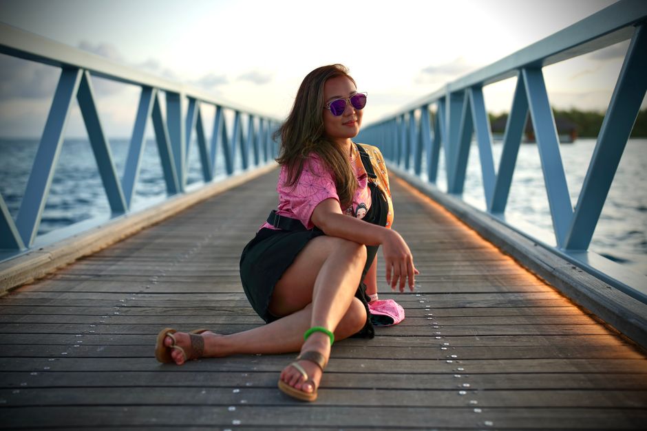 A fashionable woman poses on a boardwalk by the sea, exuding confidence and style.