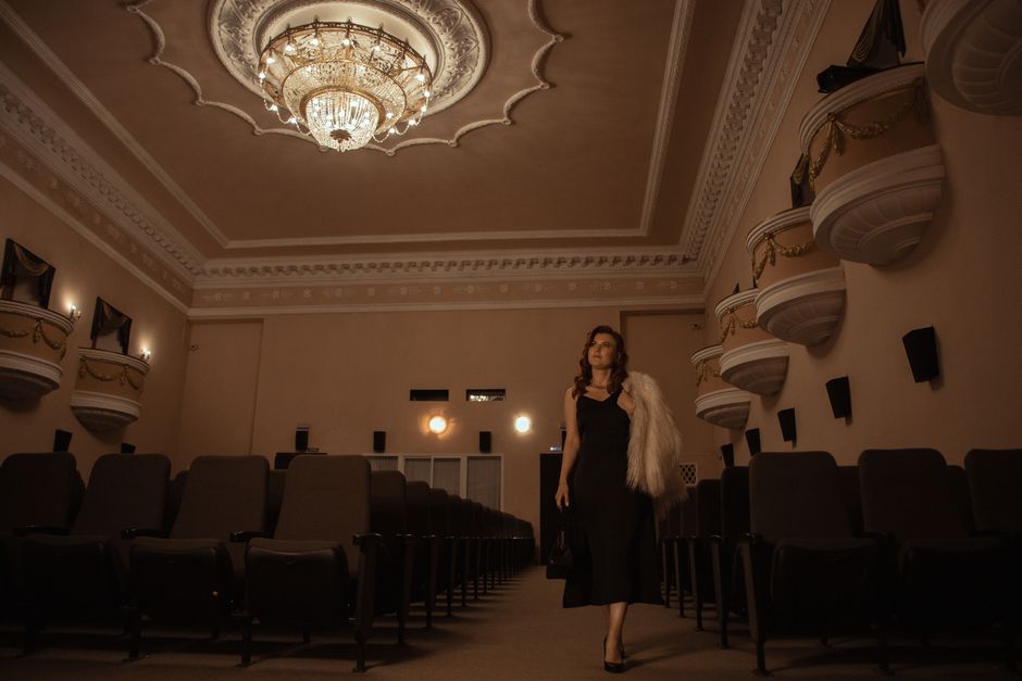 A woman in elegant attire walking through a vintage theater interior, highlighting classic architecture.