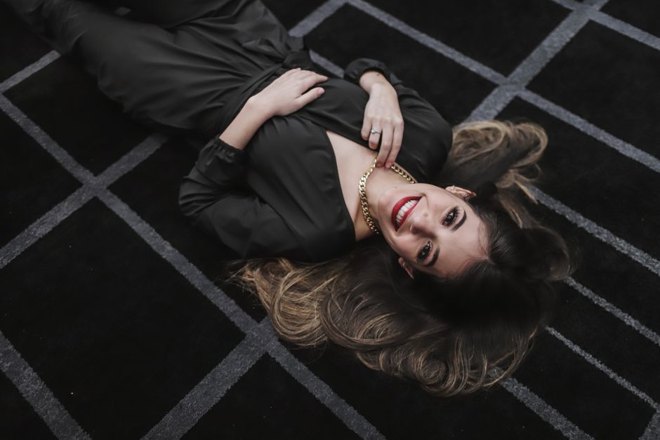 Beautiful woman in elegant attire smiling while lying on a patterned carpet indoors.