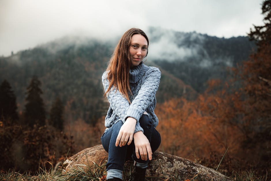 A woman in a blue sweater enjoying the misty and atmospheric autumn mountain scenery.