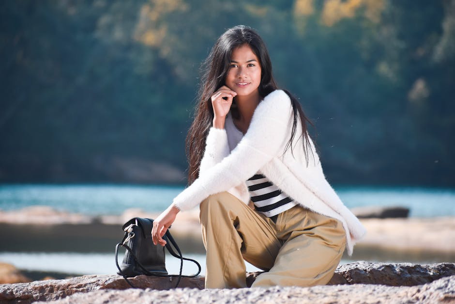 Smiling woman in brown pants and faux fur jacket posing outdoors by the water.