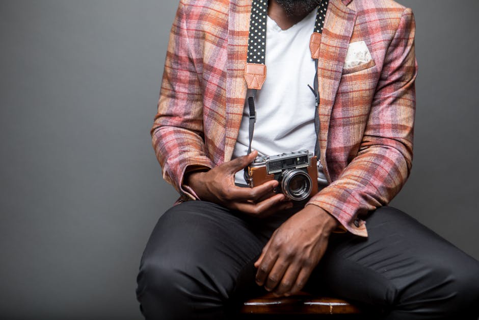 Fashionable man sitting with a classic analog camera, showcasing modern style.