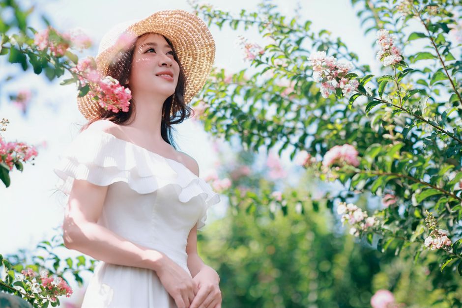 Woman in white dress and sun hat enjoying a sunny day in a blooming garden.