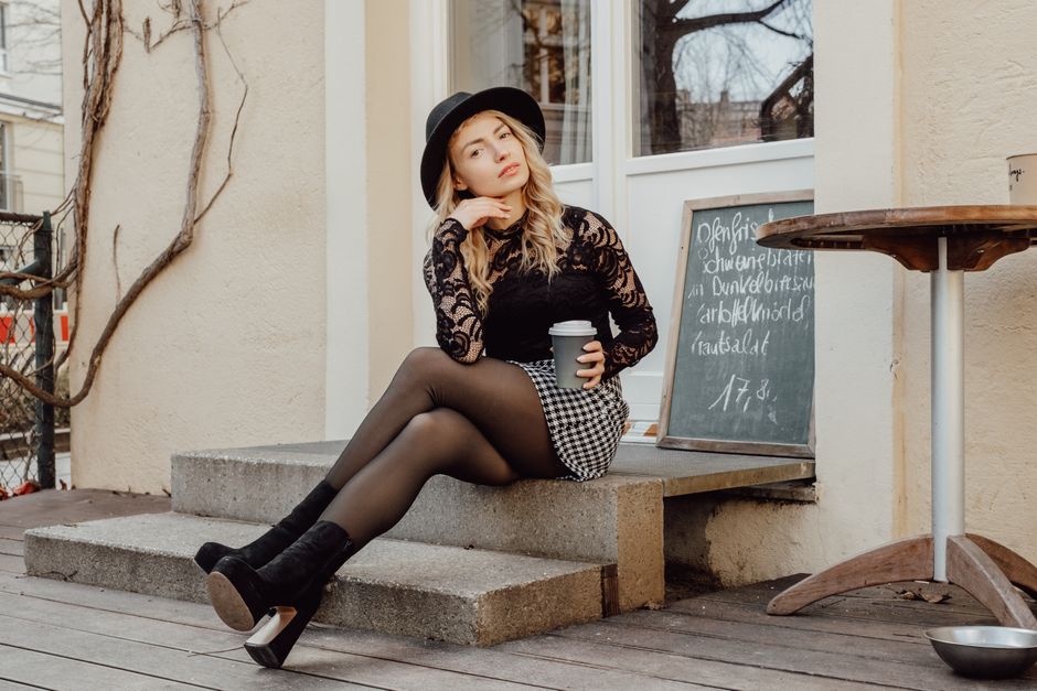 Woman in hat sitting with coffee cup on outdoor steps, chic fashion.