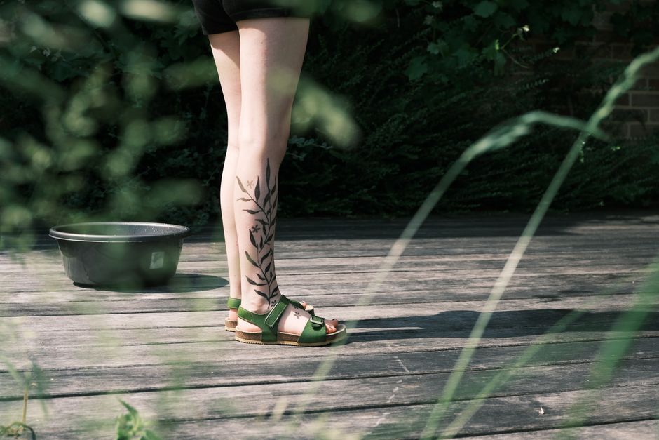 A person wearing green sandals with fern tattoo on legs, enjoying outdoors.
