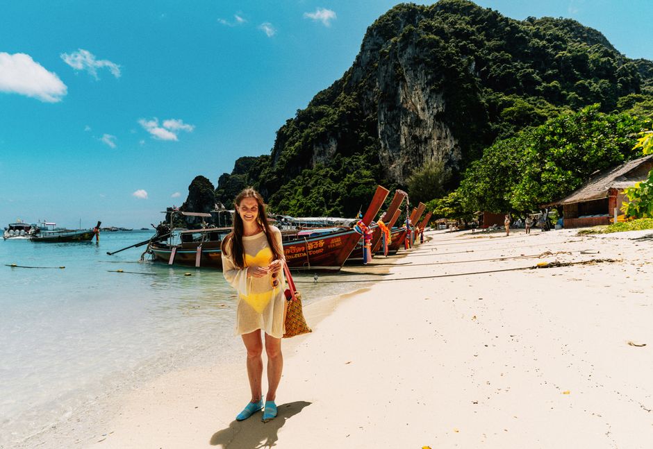 Woman enjoying a sunny day on Ko Panyi beach with traditional boats and limestone cliffs.