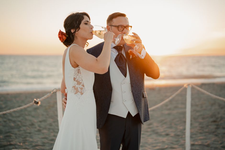 Bride and groom share a joyful sunset toast on the beach, celebrating their wedding day in style.