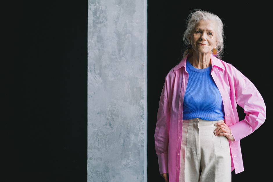 Senior woman in a vibrant outfit confidently poses indoors against a textured wall.