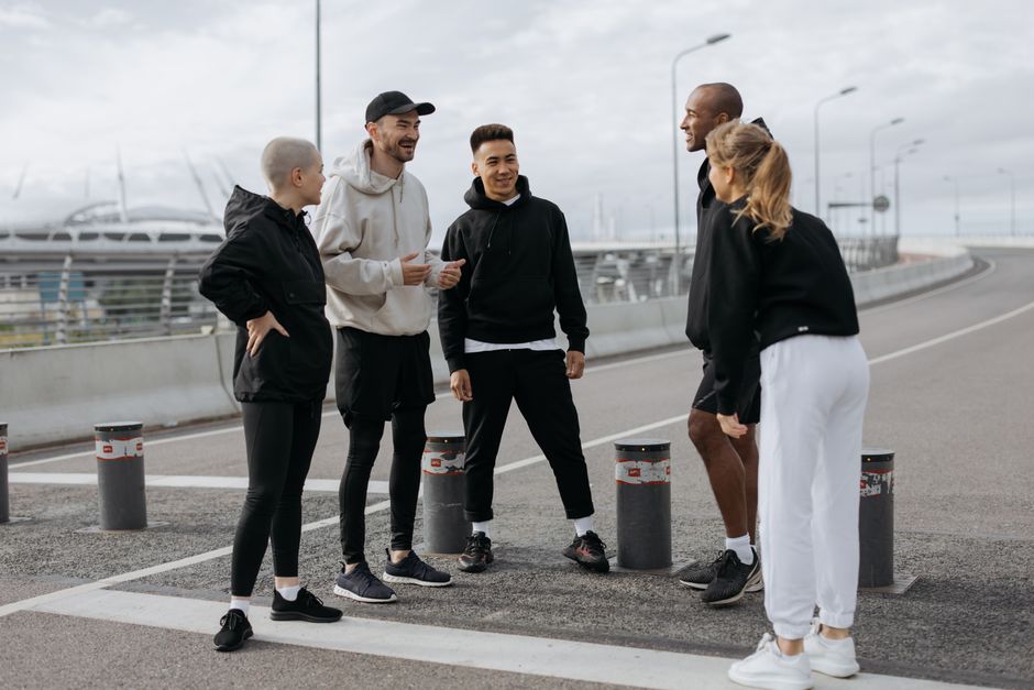 Five adults in activewear chatting on an urban street during the day.
