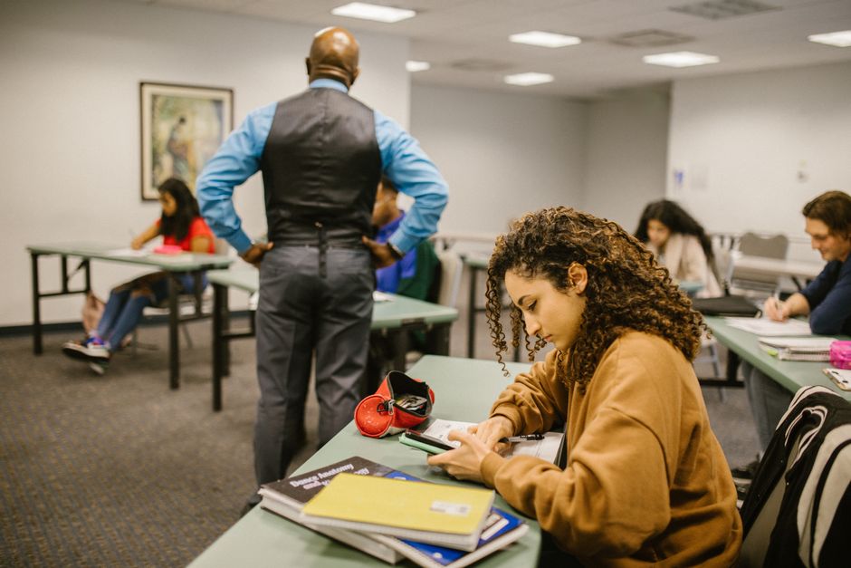 Students in a classroom setting with a teacher proctoring. Educational environment.