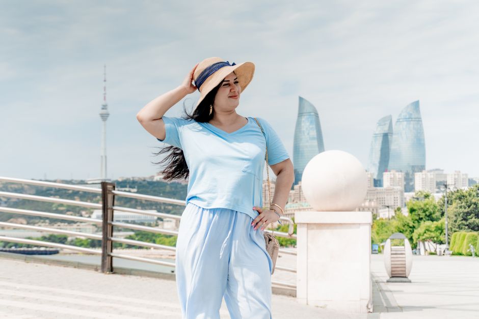 Woman in summer attire poses in front of Flame Towers in Baku, Azerbaijan, showcasing modern architecture.
