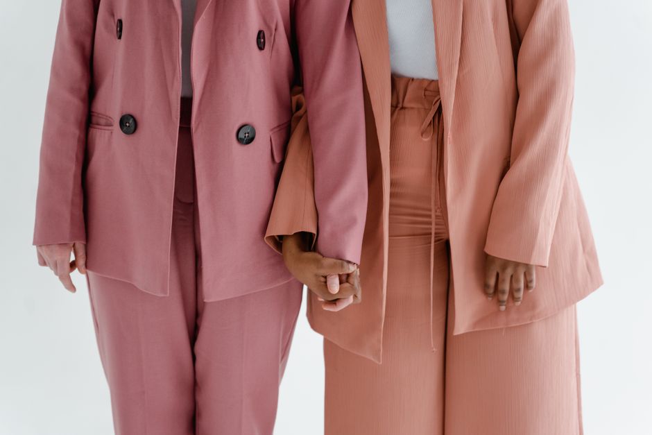 Two women in chic suits holding hands, symbolizing support and solidarity.