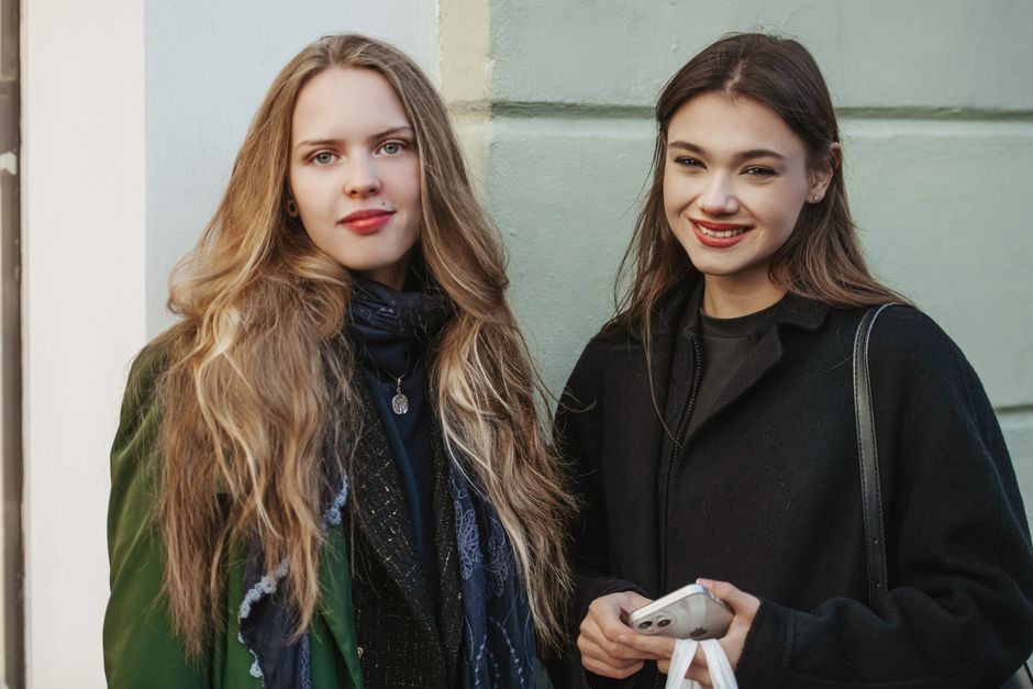 Two young women smiling in stylish coats, capturing autumn fashion and friendship.