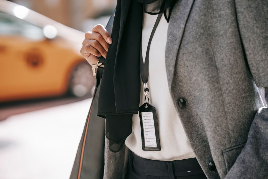 Crop unrecognizable female entrepreneur in formal outfit and name tag walking on city street on sunny day