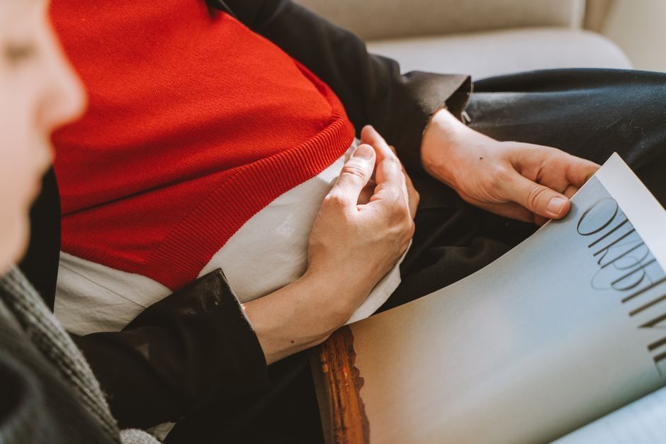 A pregnant woman sits comfortably, holding her belly and reading a magazine.
