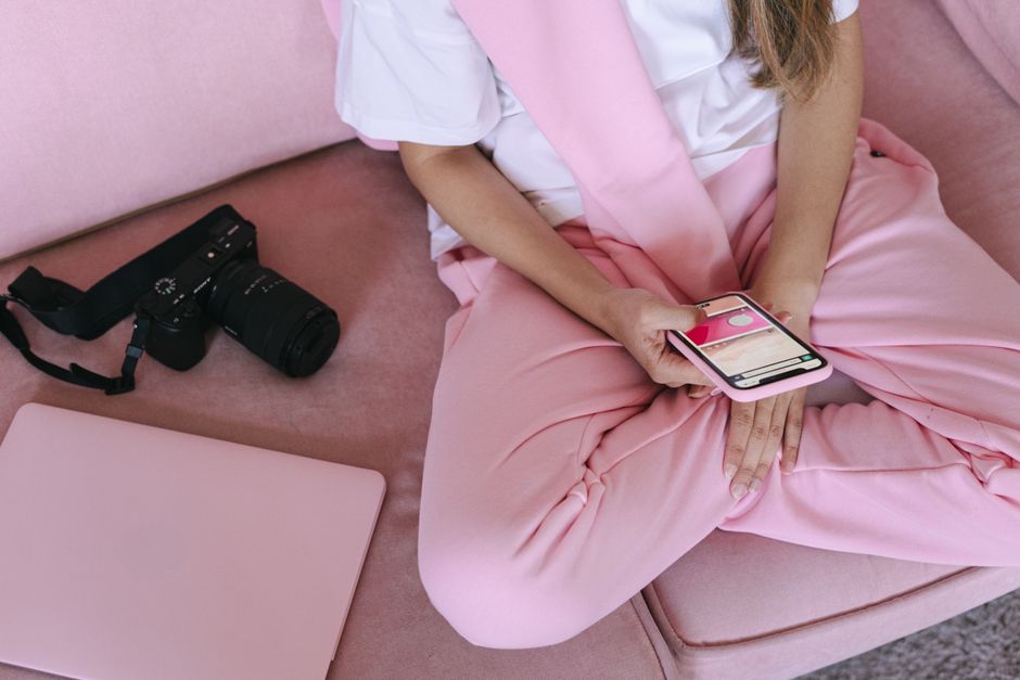 Young adult relaxing on sofa using smartphone, laptop, and camera for casual work from home setup.