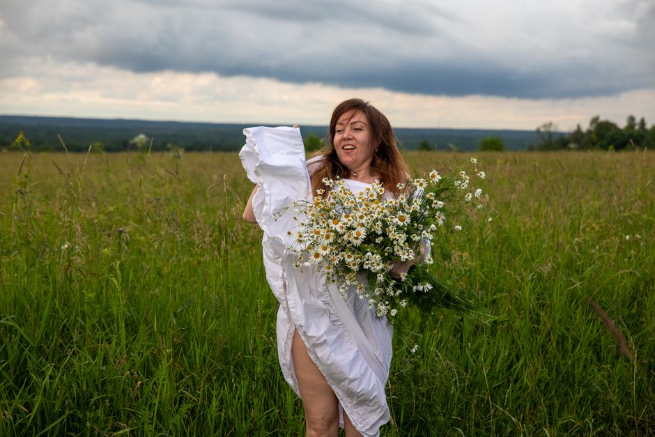 Joyful woman with daisies in a summer meadow under a cloudy sky.