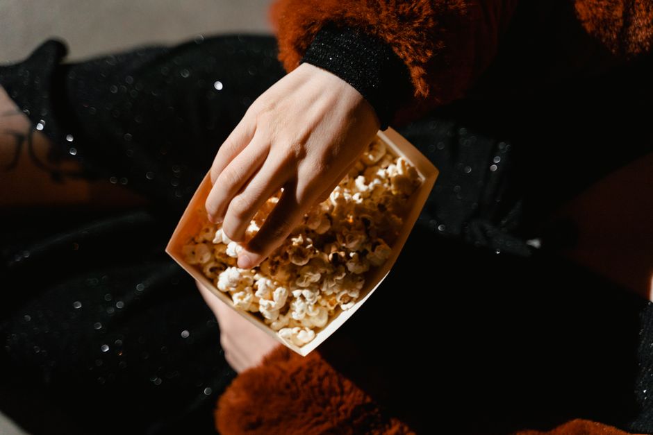 A person sitting with popcorn in a cinema, ideal for entertainment themes.