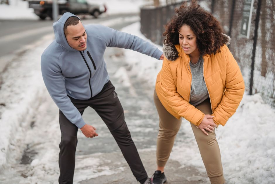 African American coach in sportswear helping plus size black female to warm up while standing on snowy pathway during training in winter time