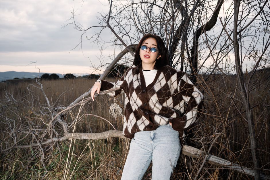 Fashionable young woman in sunglasses posing casually in a fall outdoor setting.