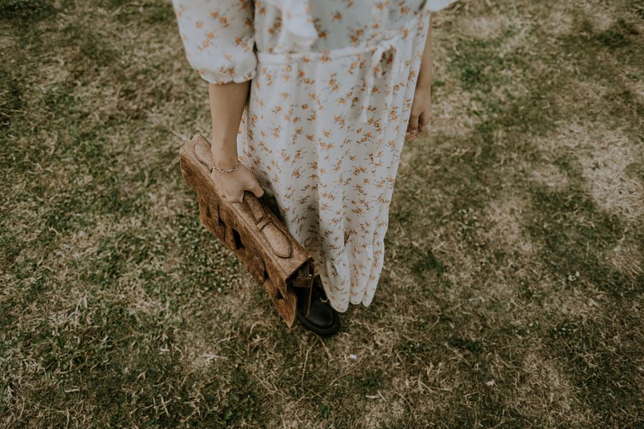 Person in floral dress holding vintage satchel on grass, summer day.