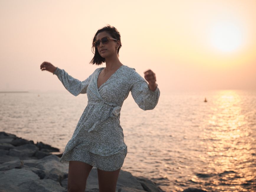 A woman in a stylish dress posing on Dubai's seashore at sunset.