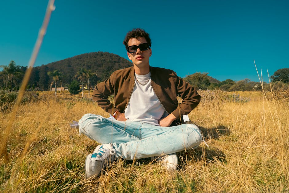 Young man in casual attire sitting outdoors in a sunny Mexican meadow, embodying a relaxed and stylish vibe.