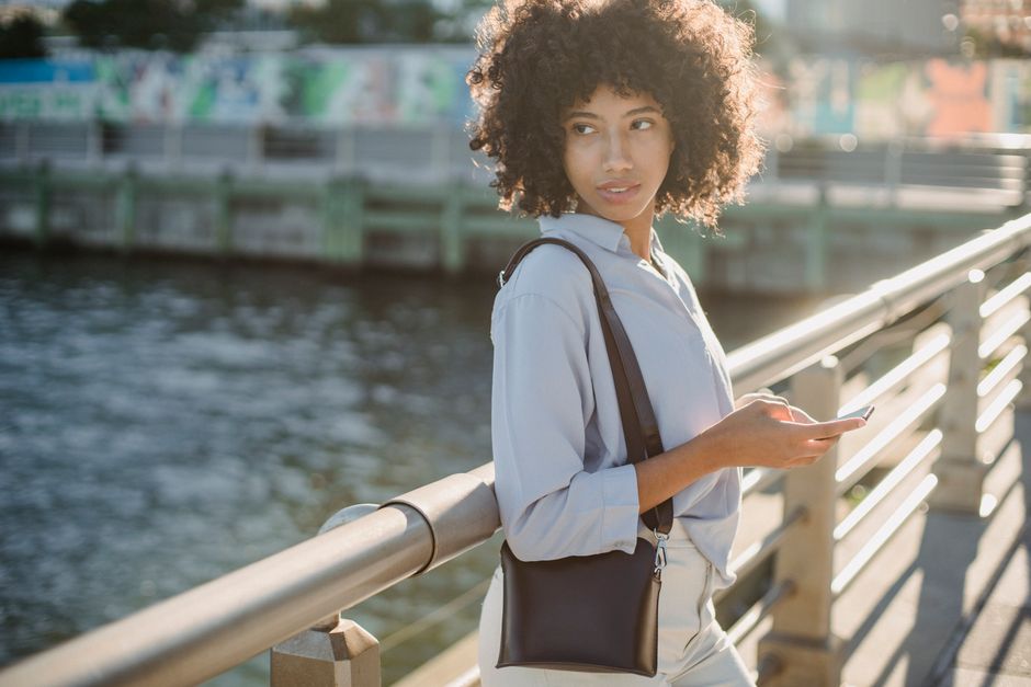 Young woman stands on bridge using smartphone in urban setting.