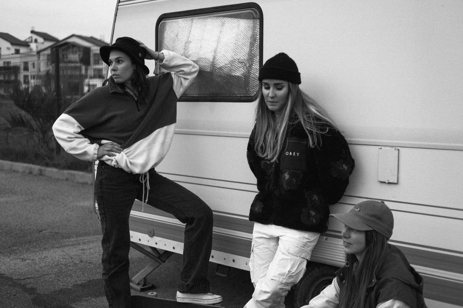 Monochrome image of three young women posing by a caravan showcasing street fashion and culture.