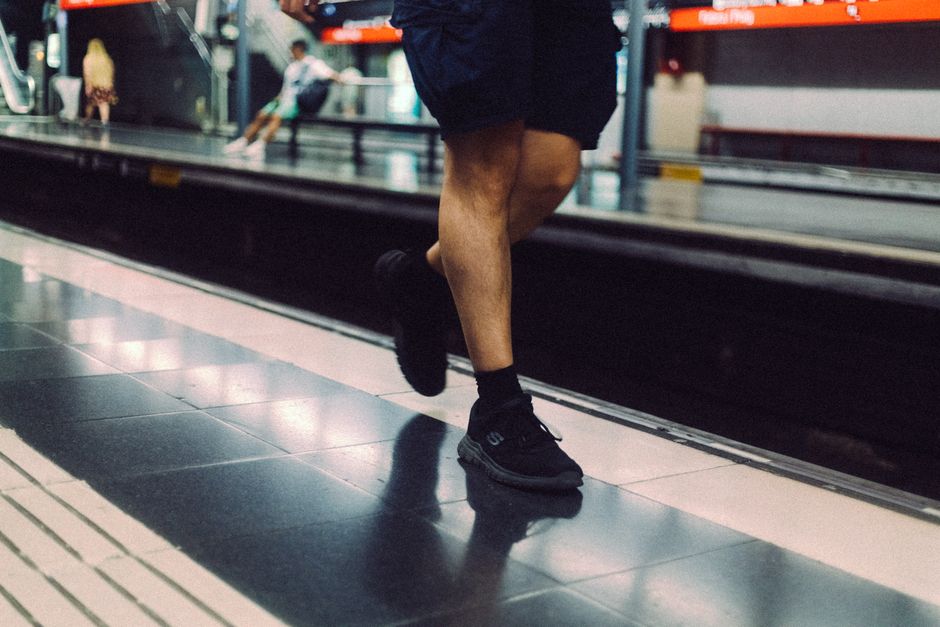 Man's legs wearing sneakers on a subway platform, urban transit scene.