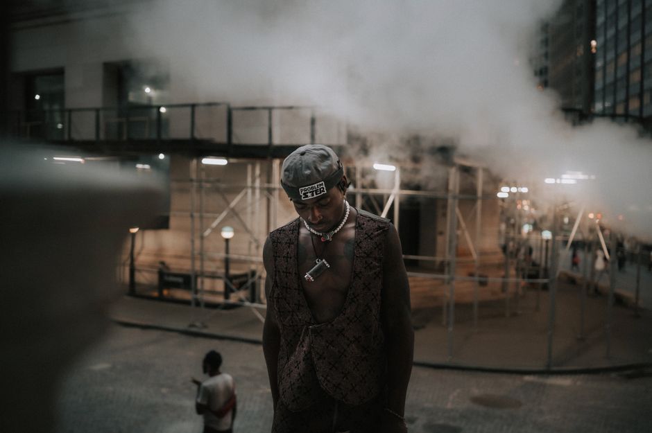 Moody portrait of a stylish man on a misty New York street at night, capturing urban fashion.