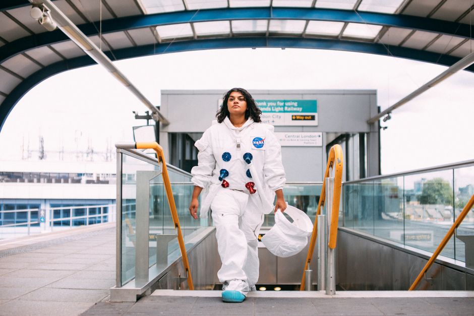A woman in a space suit walking through a London railway station, blending sci-fi and urban culture.