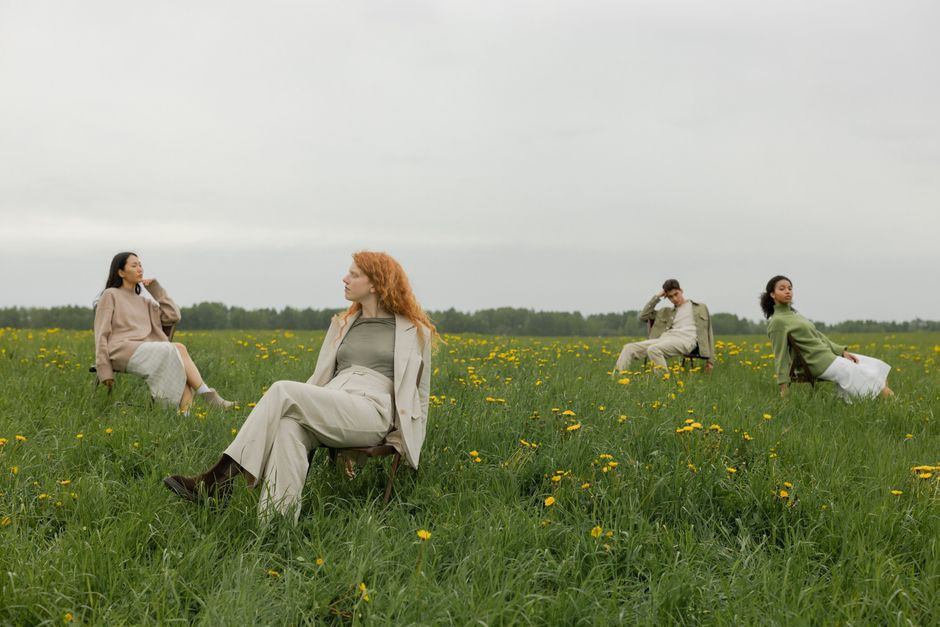 Four young adults relaxing in a green field with yellow flowers, under an overcast sky.