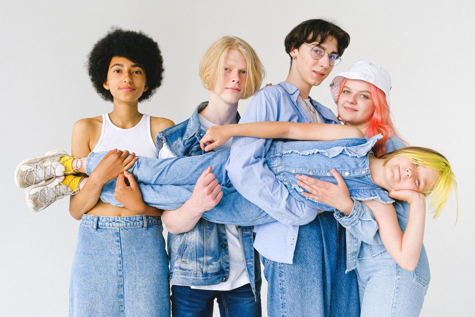 Group of cheerful multiracial teenager friends in denim clothes standing together against white background and holding girl with dyed hair and looking at camera