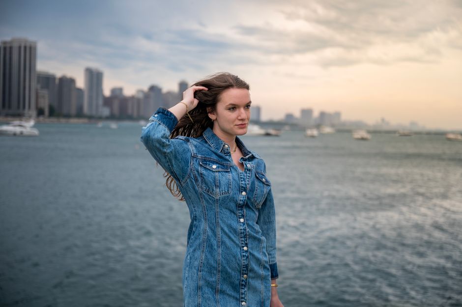 Outdoor portrait of a woman in a denim dress by the city waterfront during the day.