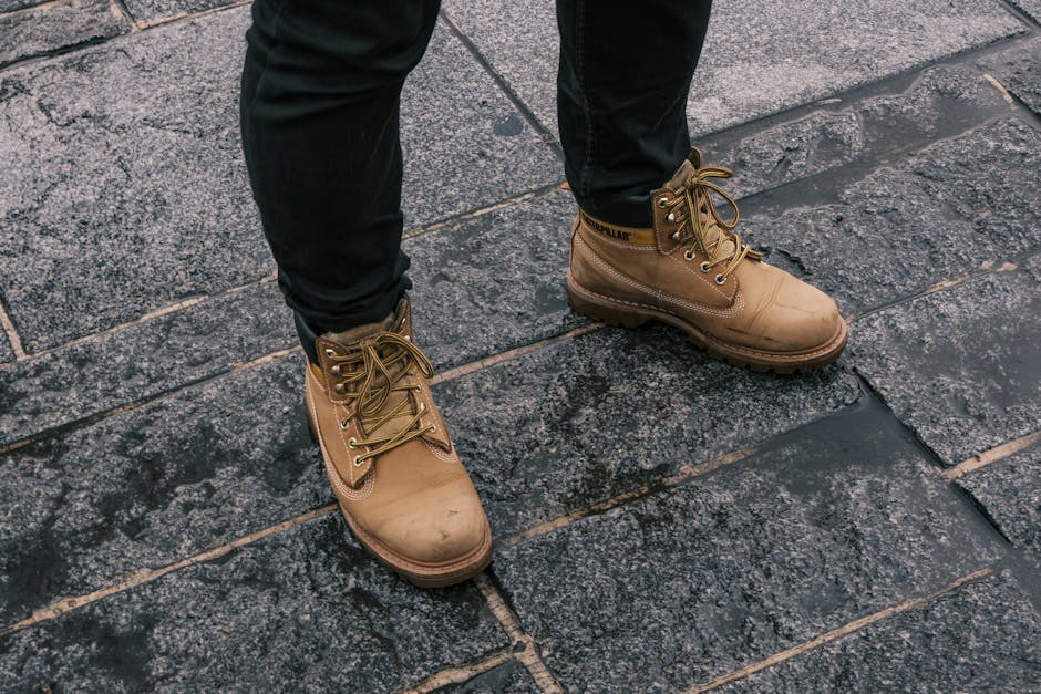 Close-up of tan work boots on wet cobblestone pavement, outdoors.