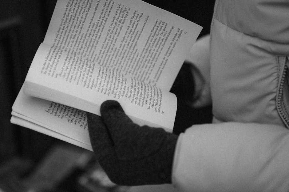Close-up of gloved hands reading a book in black and white, emphasizing literature and cozy winter vibes.
