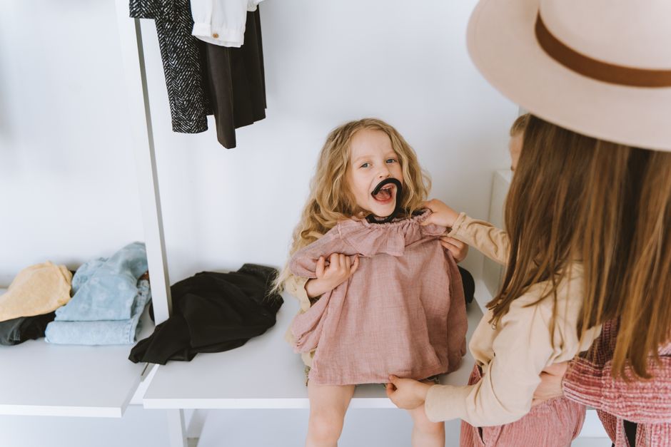 Cheerful moment of a mother helping her daughter try on a dress in a wardrobe setting.