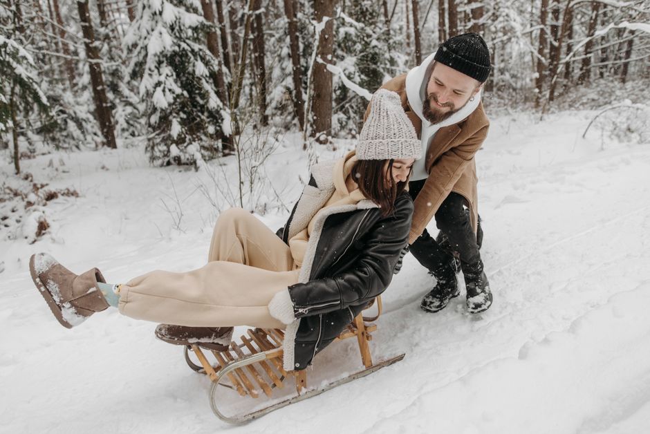 Happy couple enjoying a fun sledding experience in a snowy forest setting.